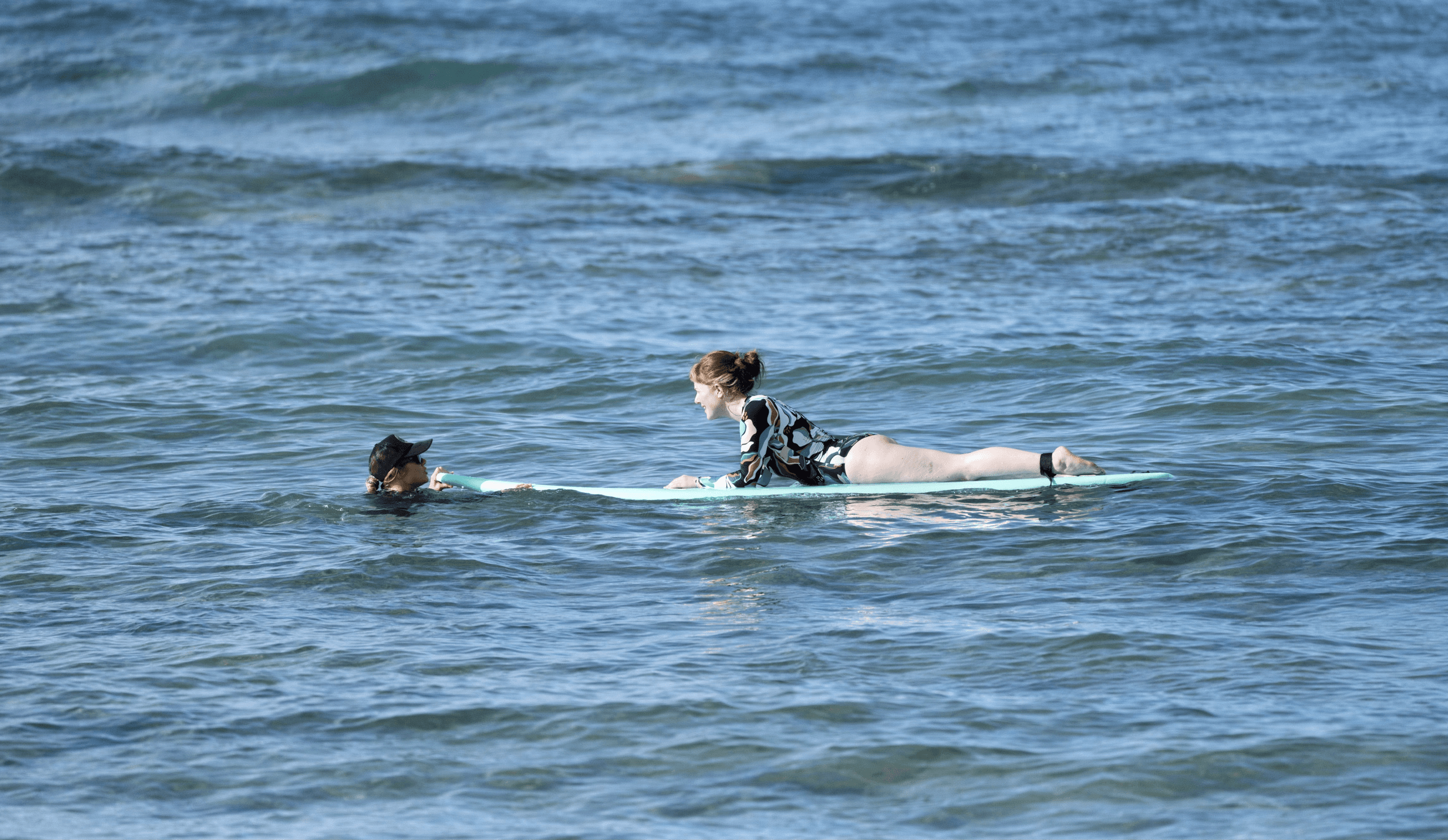 Two surfers paddling on a board in calm coastal ocean
