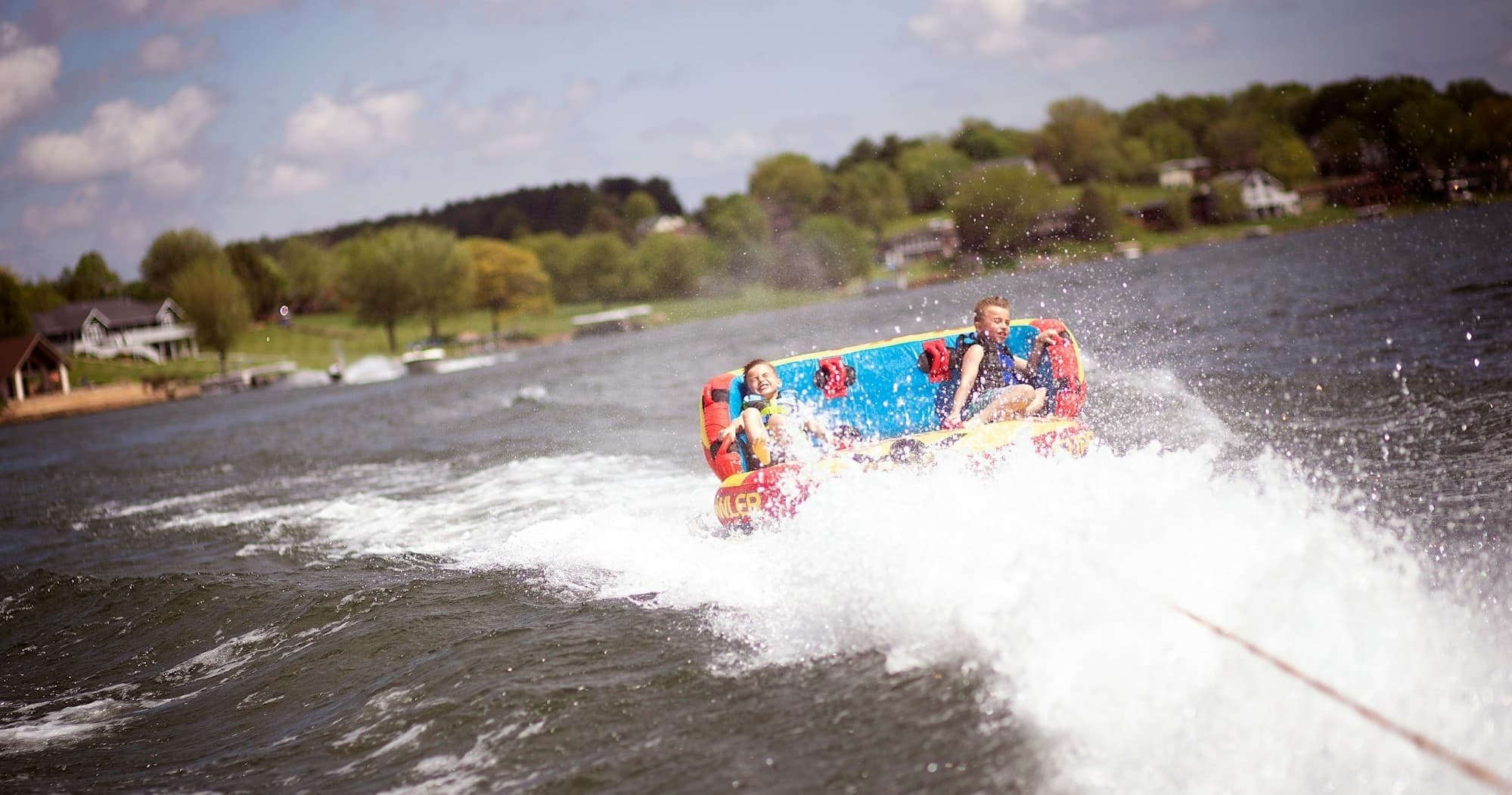 Inflatable tow tube riders bouncing through choppy lake waters near shore
