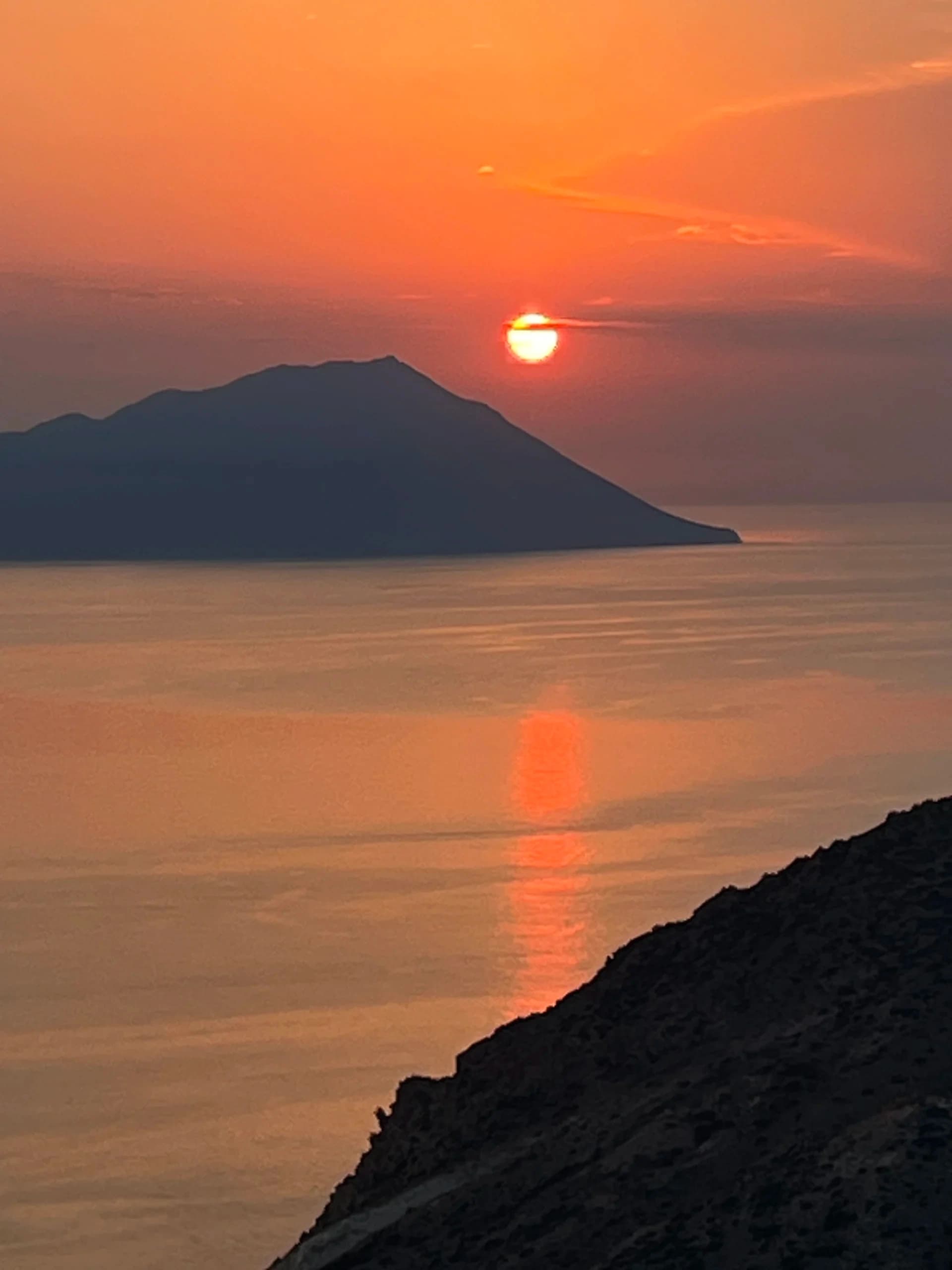 Sunset over island silhouette with reflective sea near Milos coastline