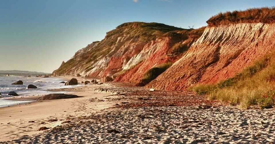 Sandy pebble beach and red cliffs along scenic island coastline