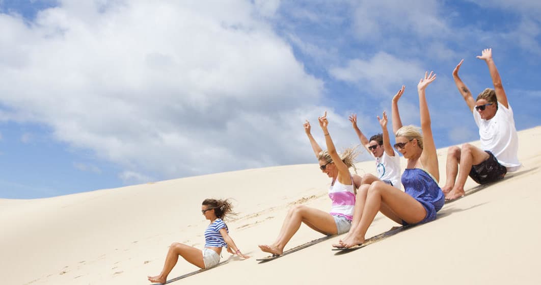 Friends sliding down sandy dunes enjoying 4WD beach tour