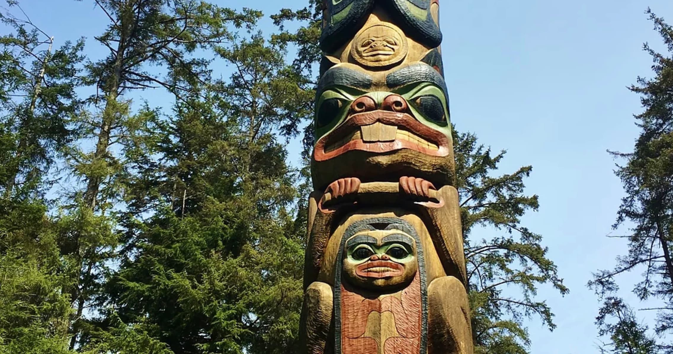 Carved totem pole among evergreen trees on coastal trail