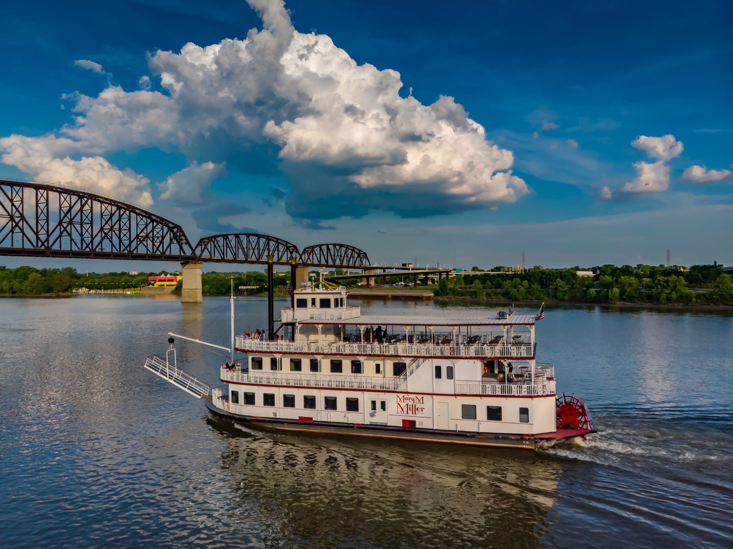 Historic steamboat cruising Ohio River with blue skies and bridge