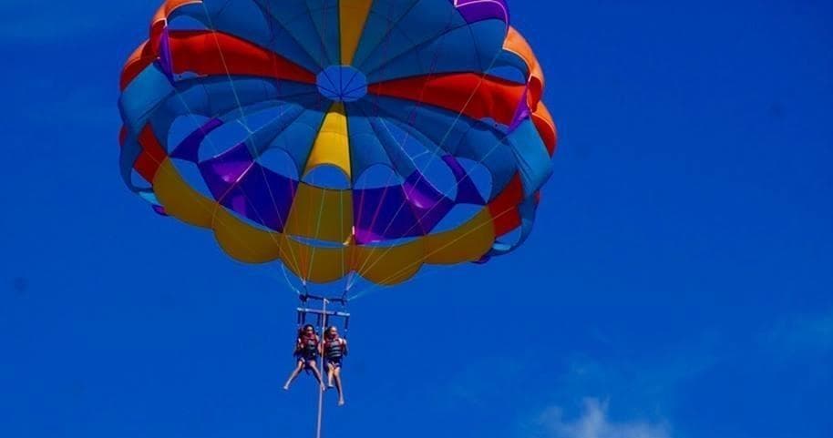 Two parasailers under colorful canopy over deep blue ocean sky