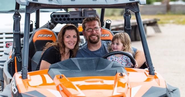 Family riding orange UTV on desert trail, guided off-road tour