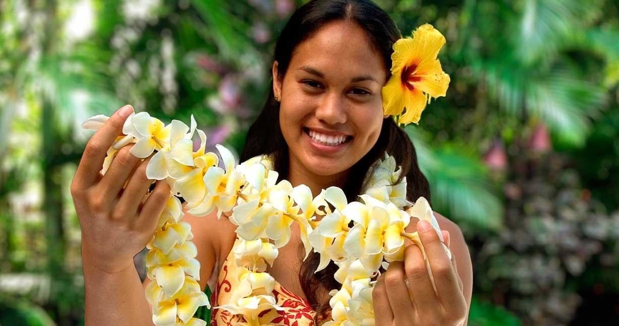 Woman presenting plumeria lei in tropical garden setting