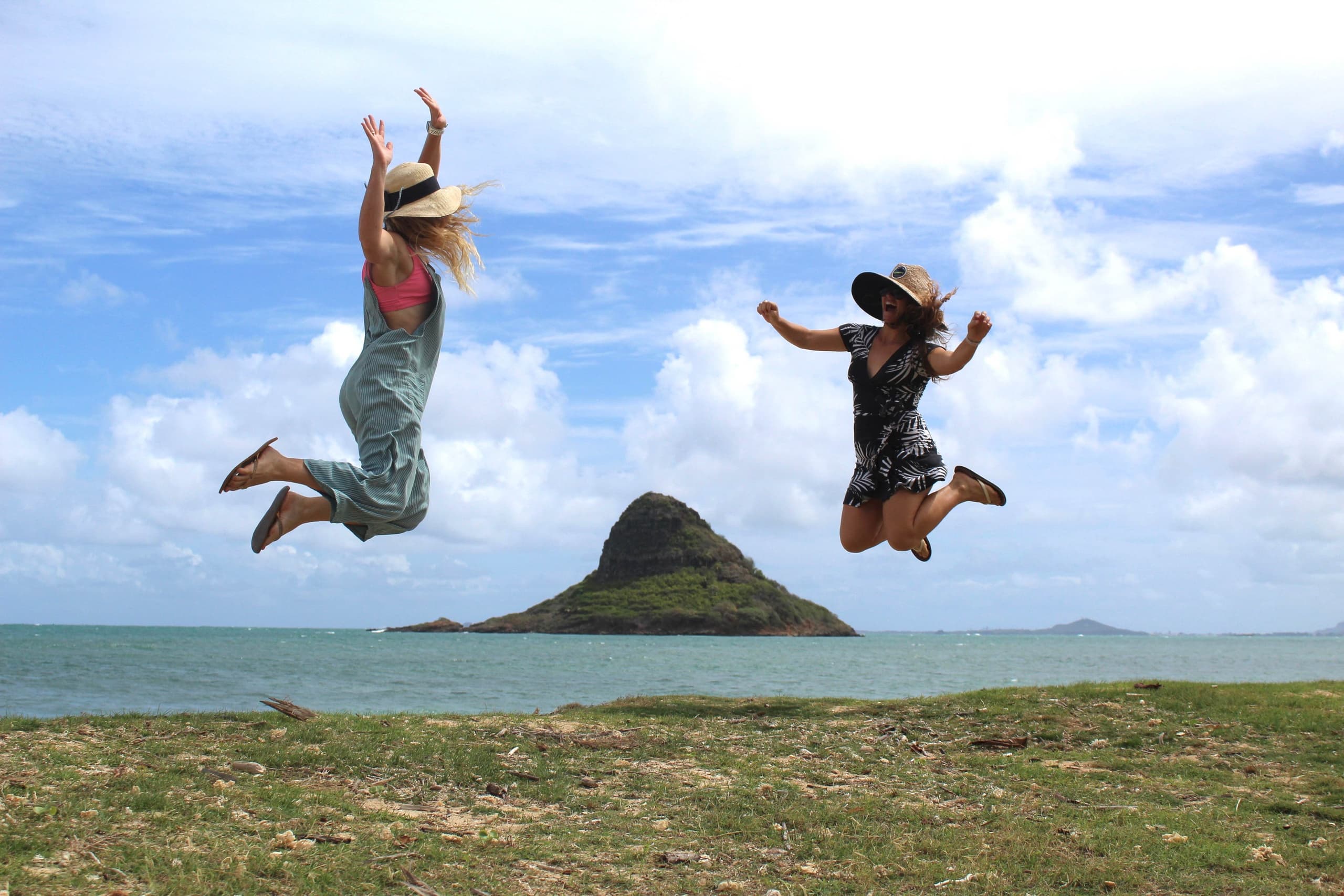 Friends jumping on coastal grass with Mokulua islets and ocean
