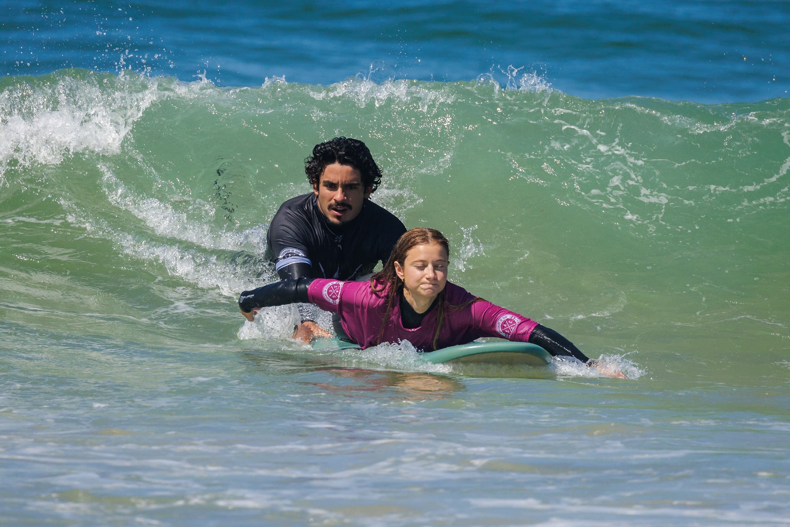 Instructor guiding student paddling on surfboard through breaking wave