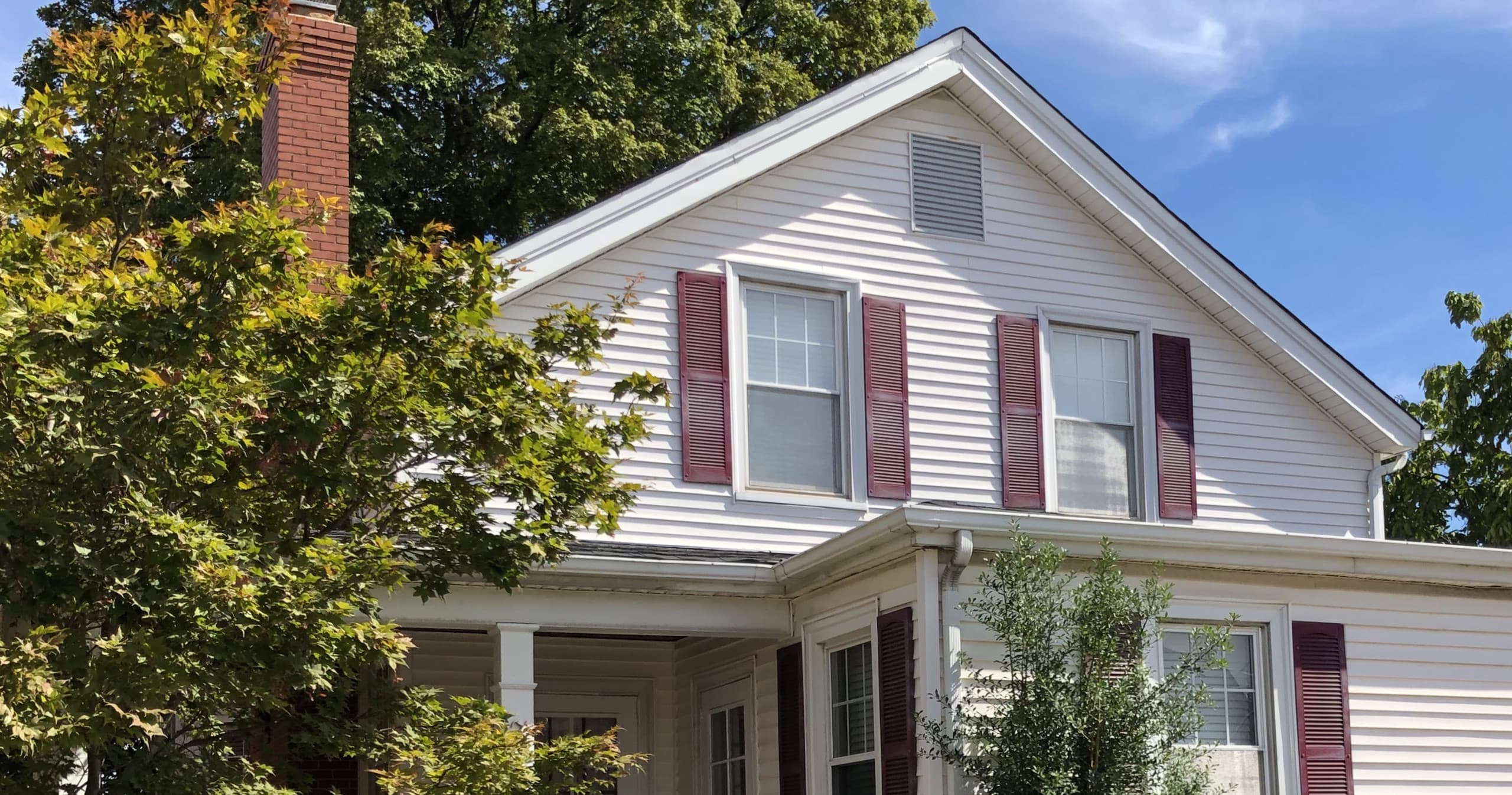 Historic cottage exterior with porch and mature trees outdoors