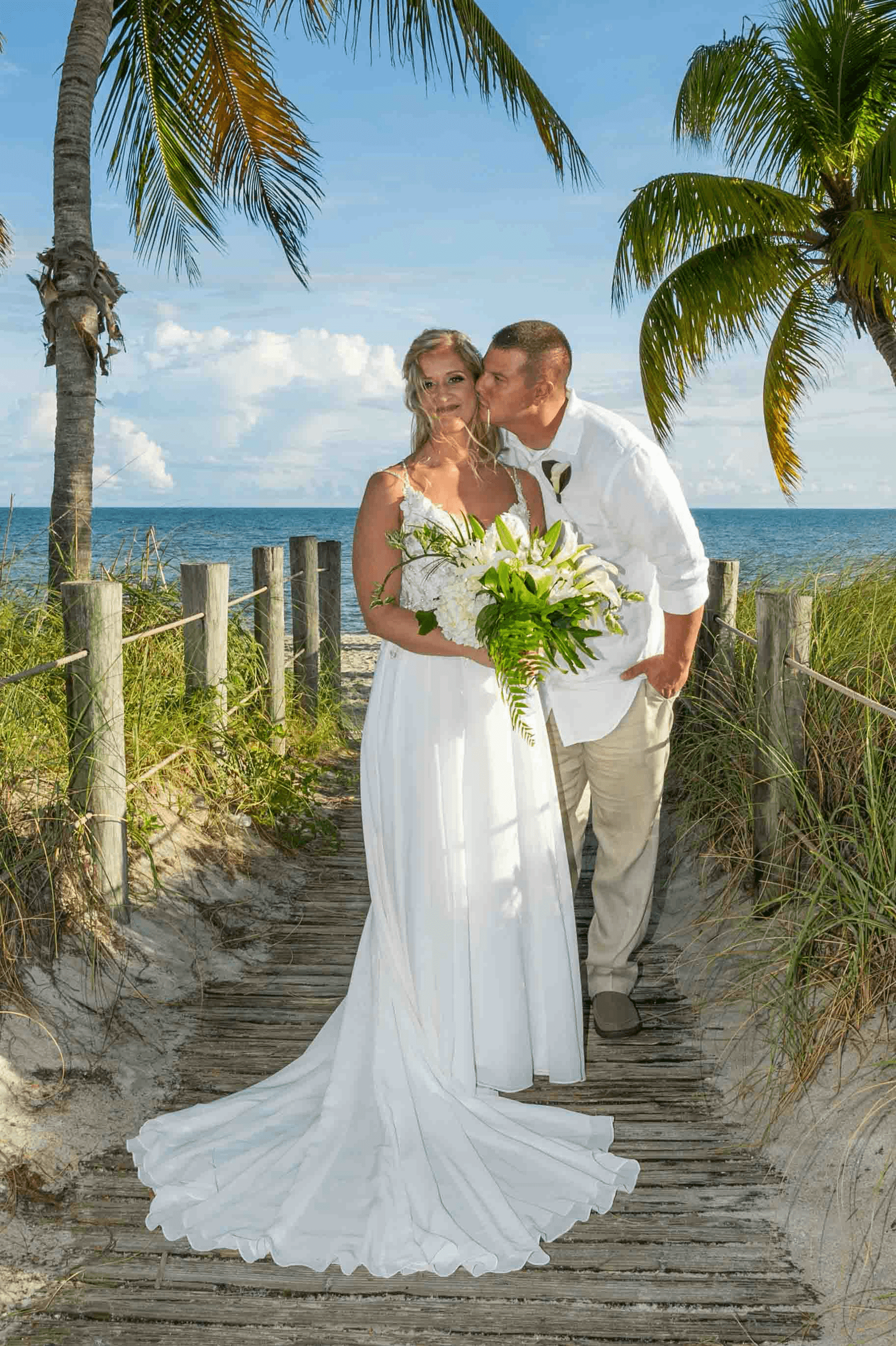 Bride and groom posed on palm-lined boardwalk by the ocean