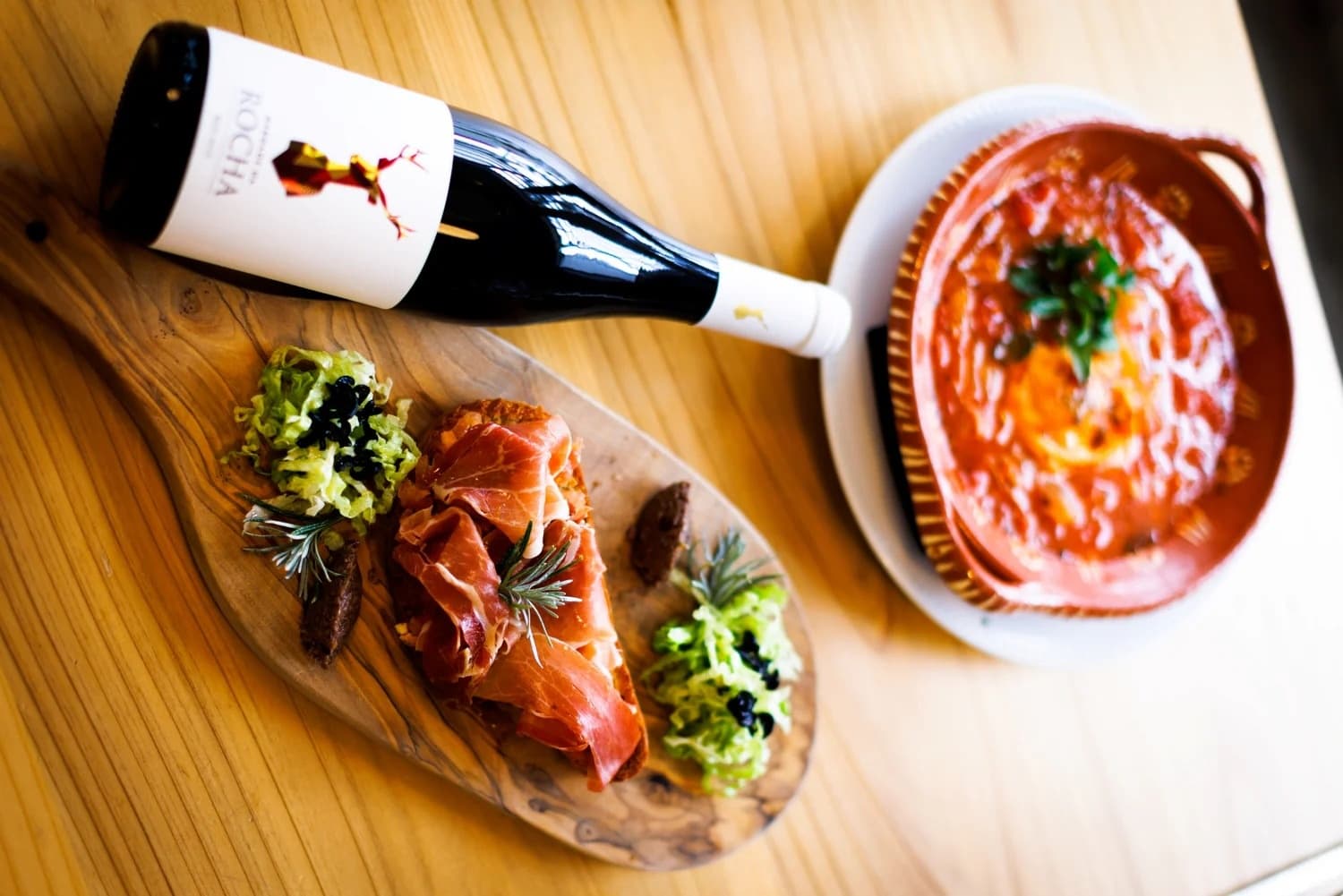 Wine bottle, tapas and bowl of tomato stew on indoor wooden table