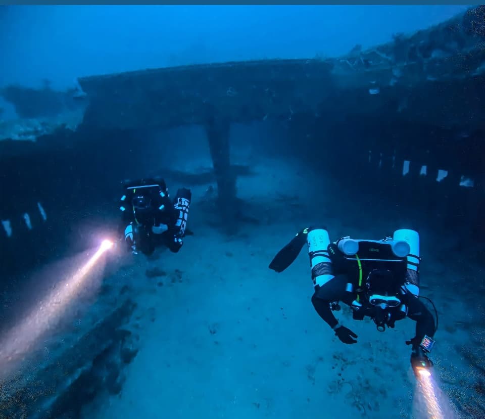 Pair of scuba divers exploring sunken shipwreck with torches