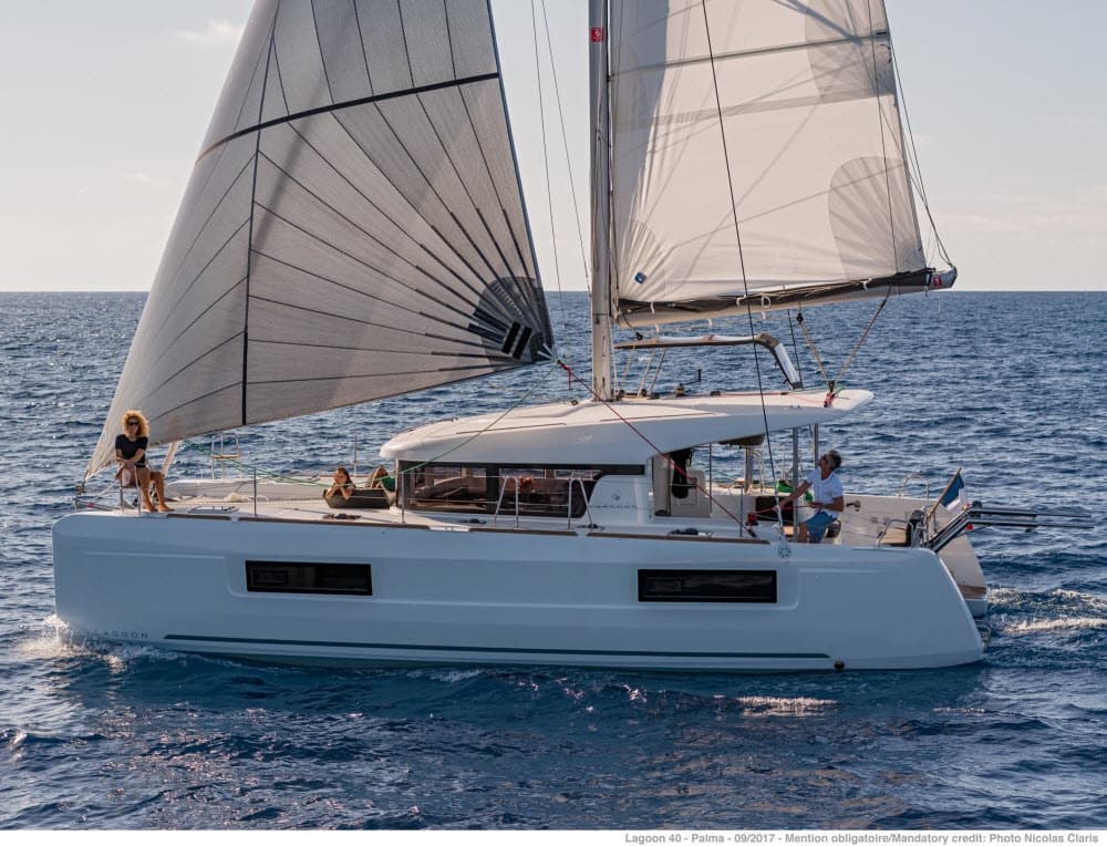 Catamaran sailing on open ocean at sunset with guests