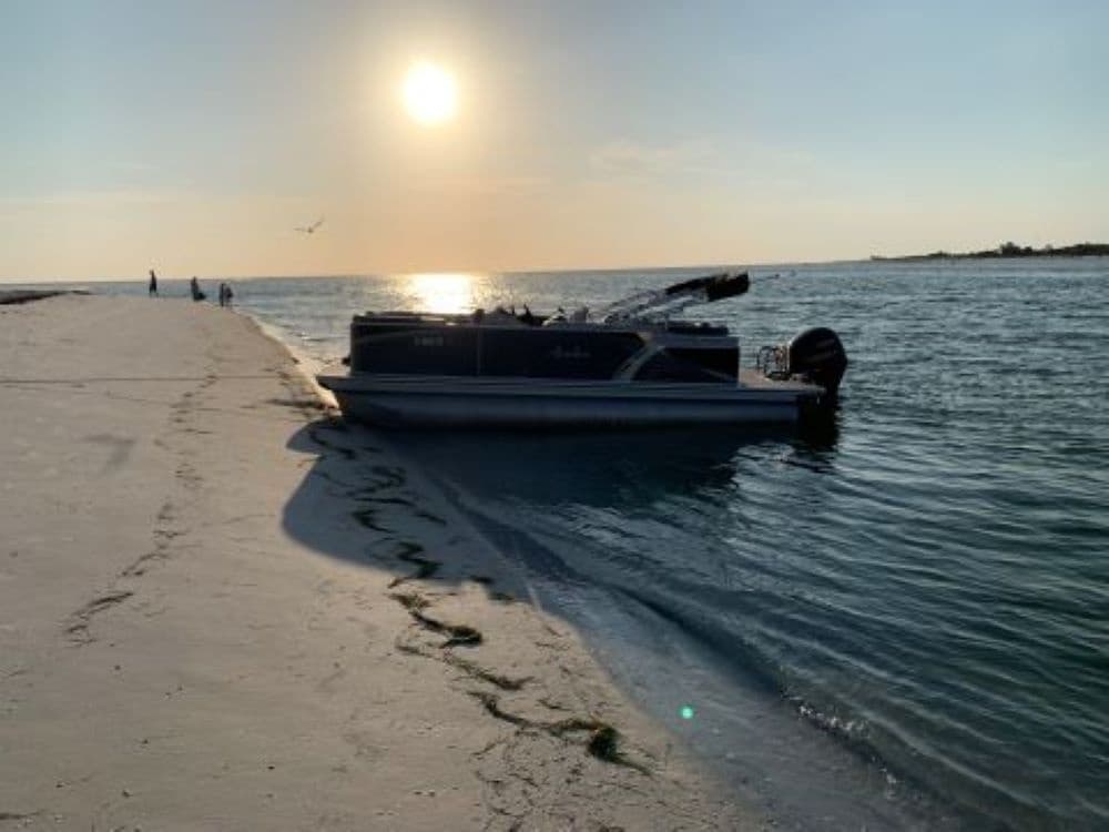 Pontoon boat anchored near sandy shore at sunset on calm bay