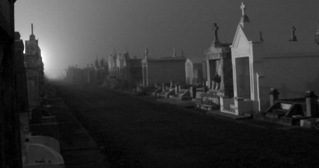 Foggy cemetery row at dawn with moody mausoleums, haunted feel