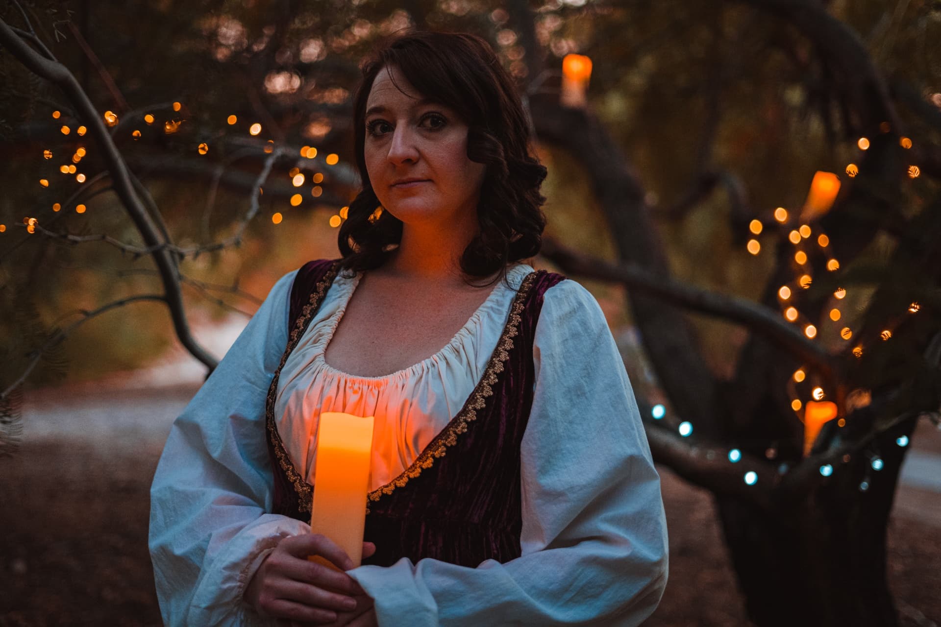 Woman in Renaissance costume holding candle at dusk outdoors