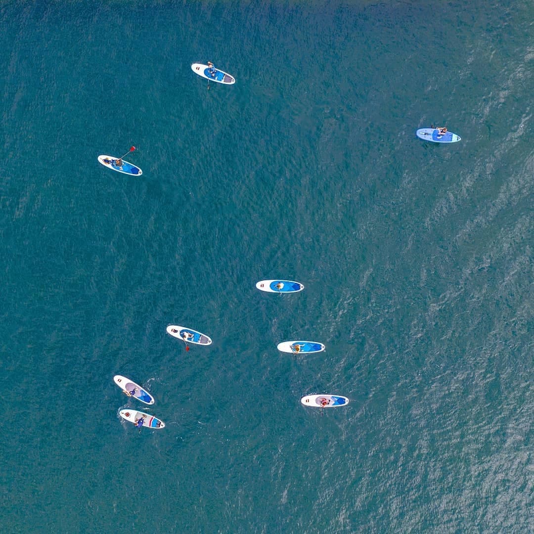 Aerial view of paddleboarders scattered on open teal ocean