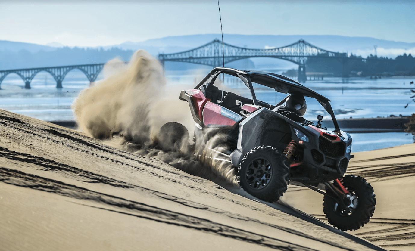 Side-by-side UTV powering up sandy riverbank with bridge backdrop
