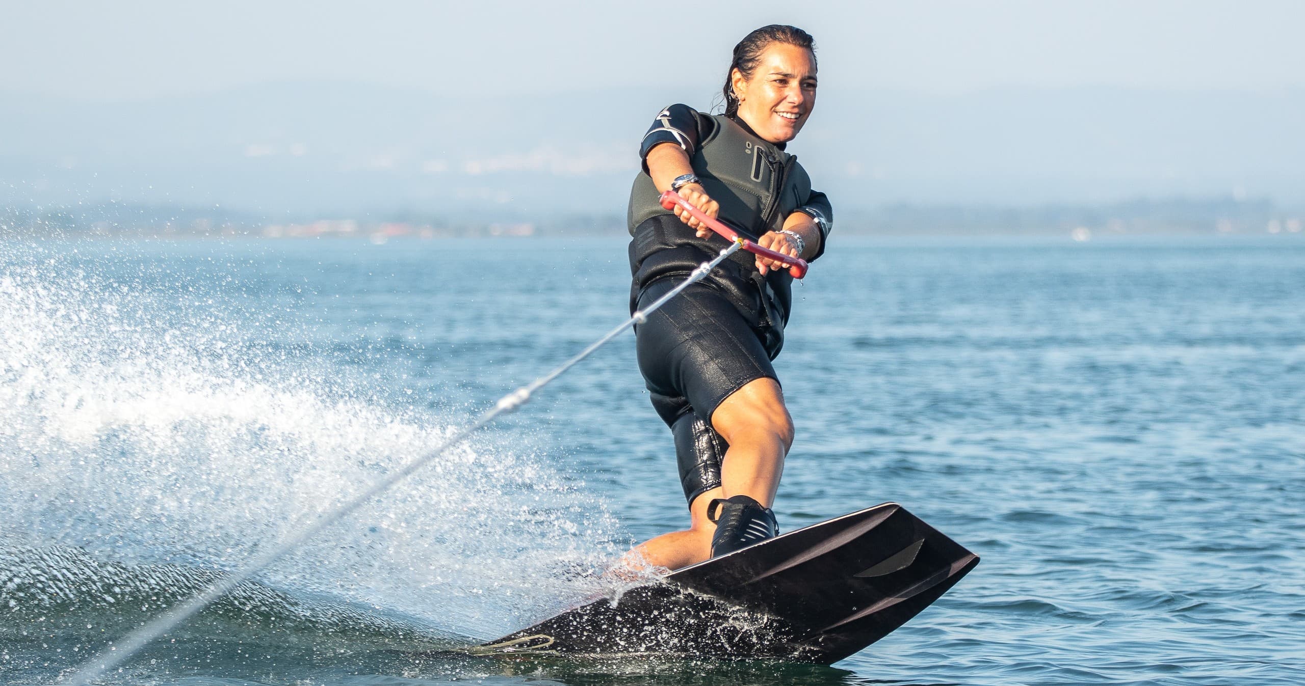 Wakeboarder carving high spray across blue coastal waters