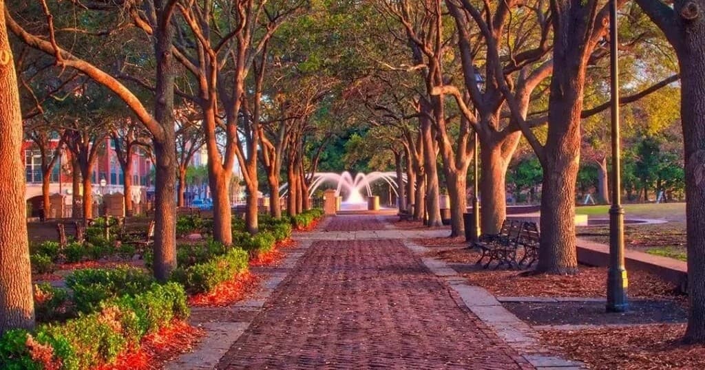 Sunlit tree-lined brick promenade leading to park fountain