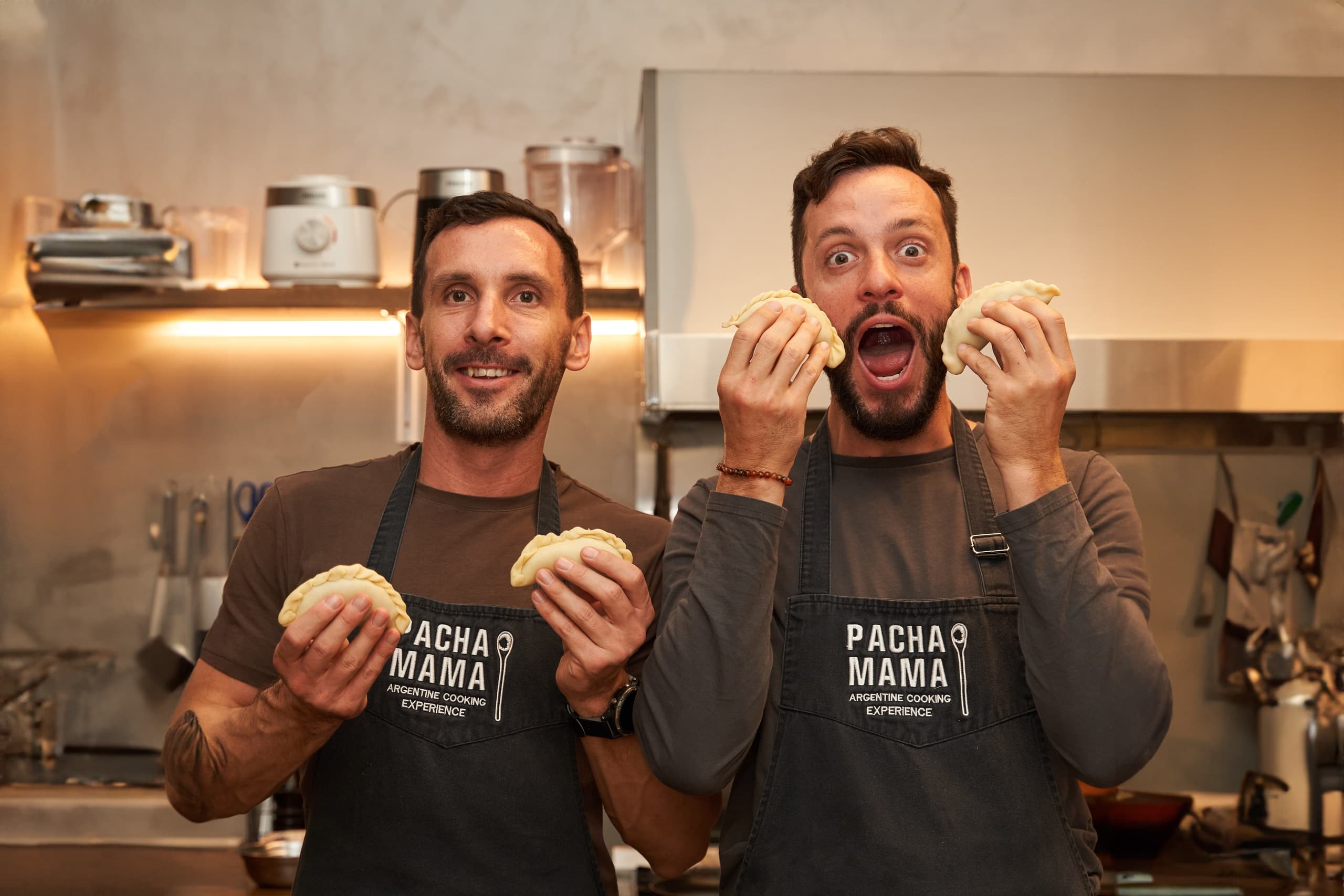 Two chefs holding arepas in kitchen during cooking demo