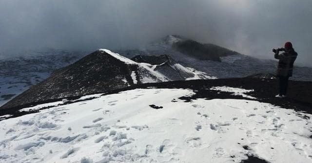 Solo trekker photographing snowy crater rim with foggy vista, Sicily