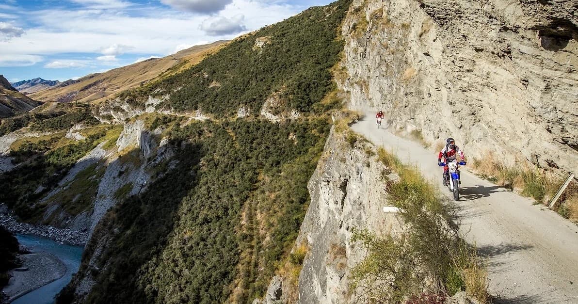 Motorcyclist on narrow cliffside gravel road with canyon views