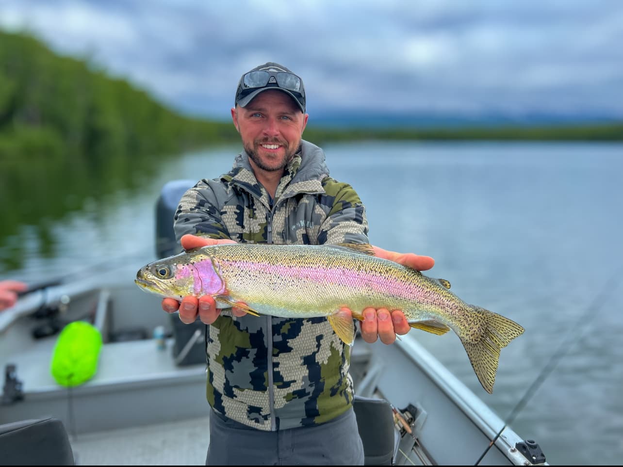 Angler holding rainbow trout on lake boat in scenic wilderness