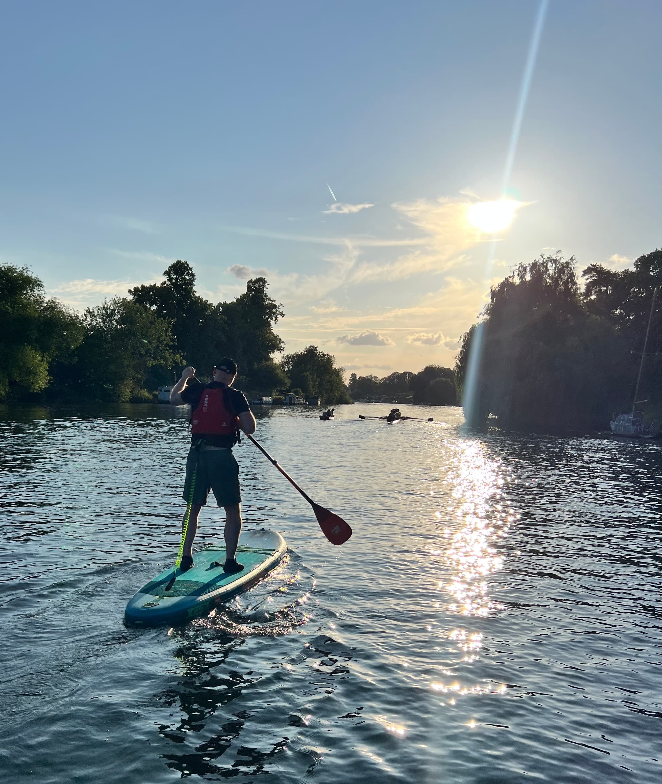 Stand-up paddler silhouetted at sunset on reflective river