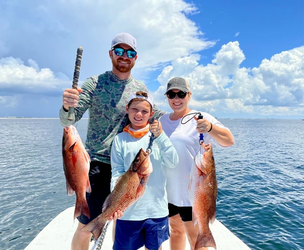 Family posing with red snapper catches under blue sky off Destin