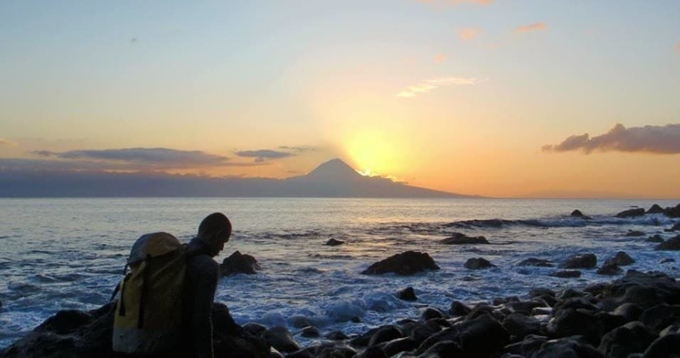Backpacker watching sunset over rocky Atlantic shore at dusk