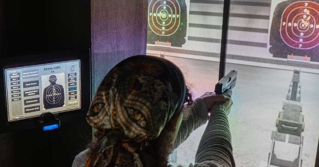 Shooter firing handgun at indoor range target during training simulation