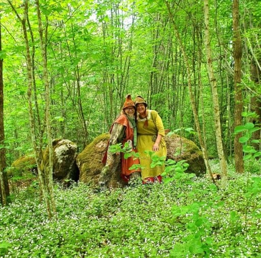 Two hikers posing in dense green forest among wildflowers and boulders