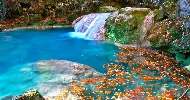 Hikers exploring turquoise waterfall pools in forest canyon
