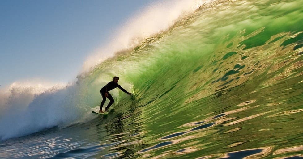 Surfer riding emerald barrel wave on scenic Pacific coast