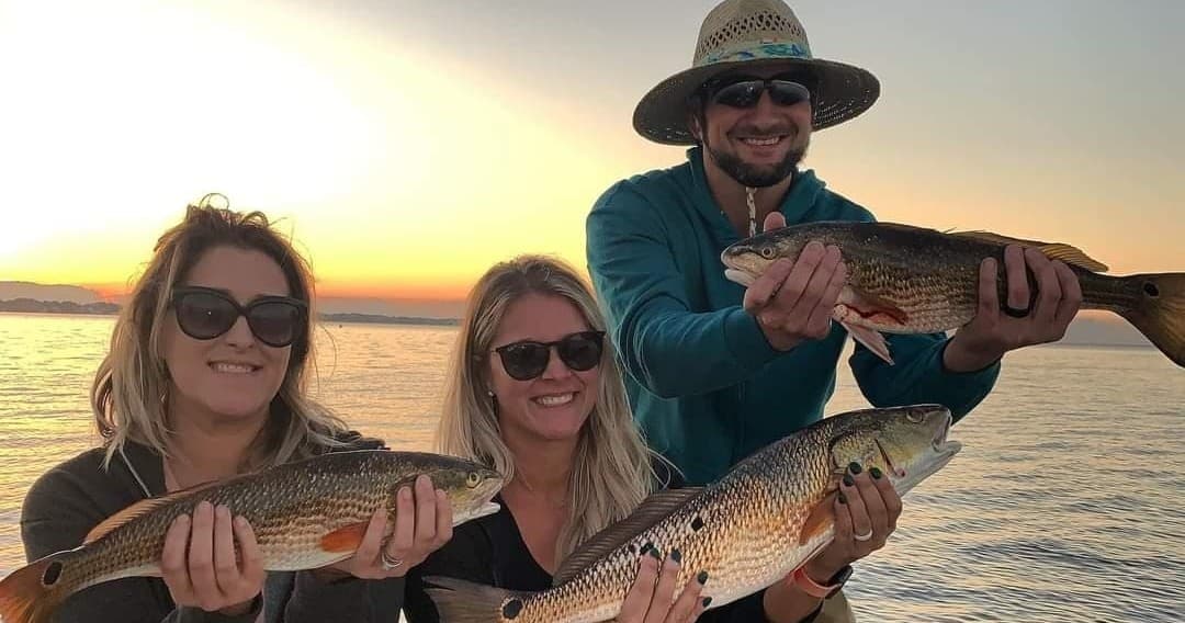 Group holding redfish at sunset on coastal fishing charter
