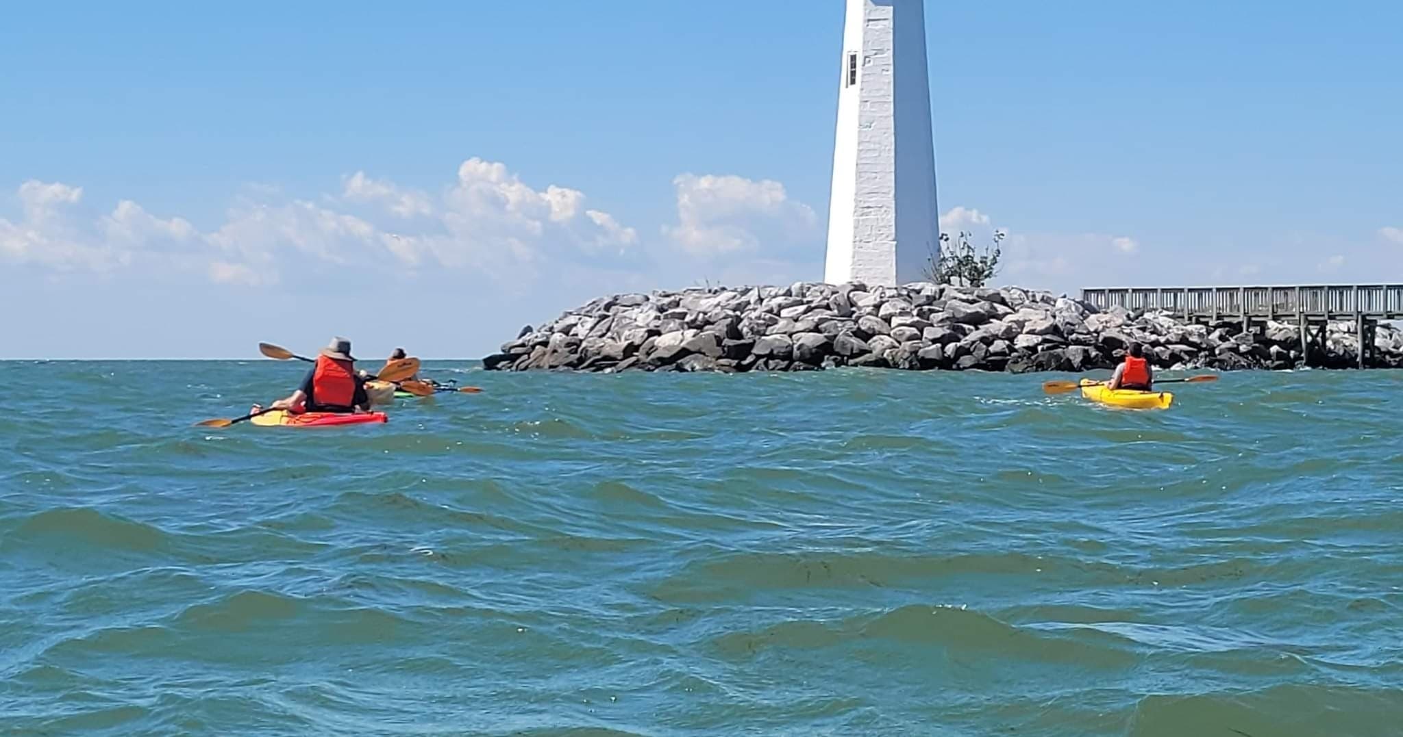 Kayakers paddling toward lighthouse on bright coastal waters
