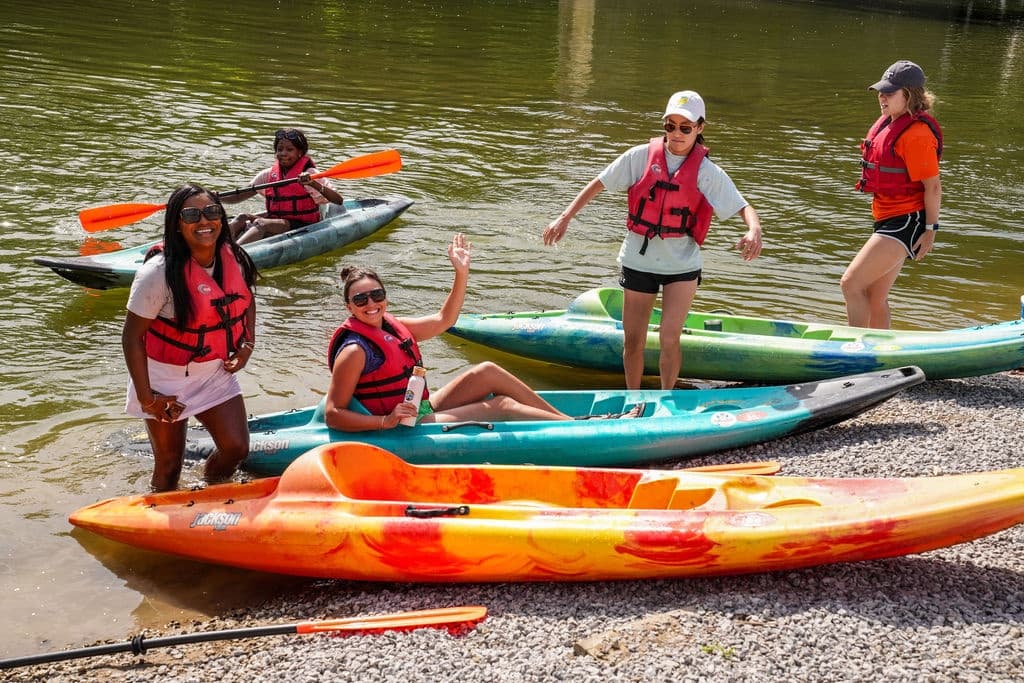Group of kayakers launching from riverbank, wearing life jackets