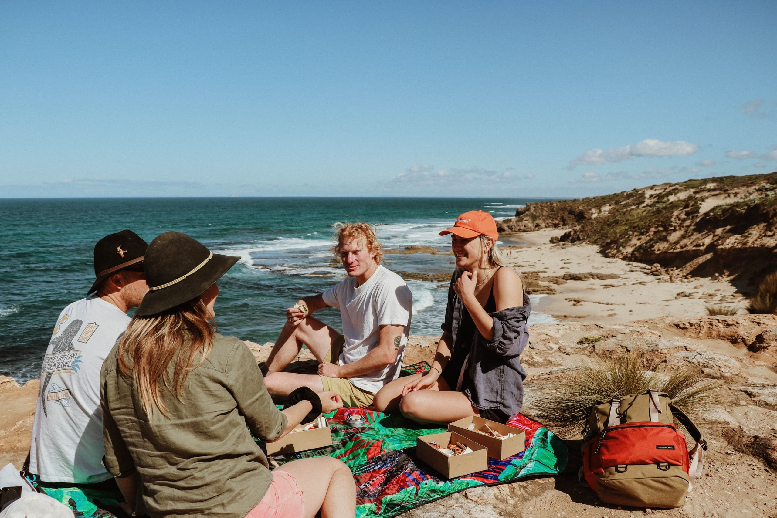 Friends picnic on coastal cliffs with ocean views, outdoor meetup