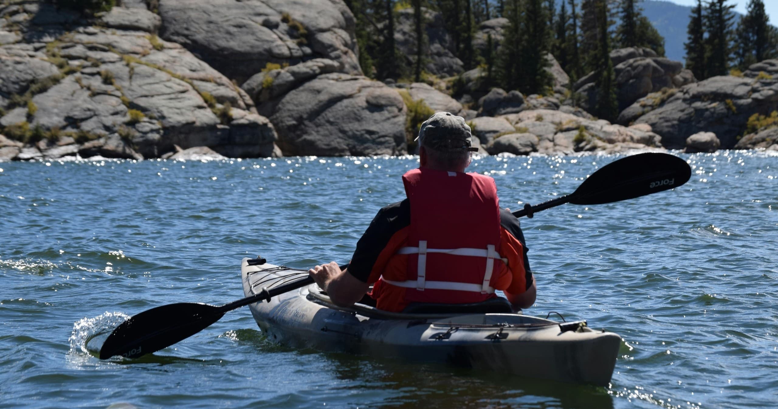 Kayaker paddling near rocky shoreline in open lake scenery