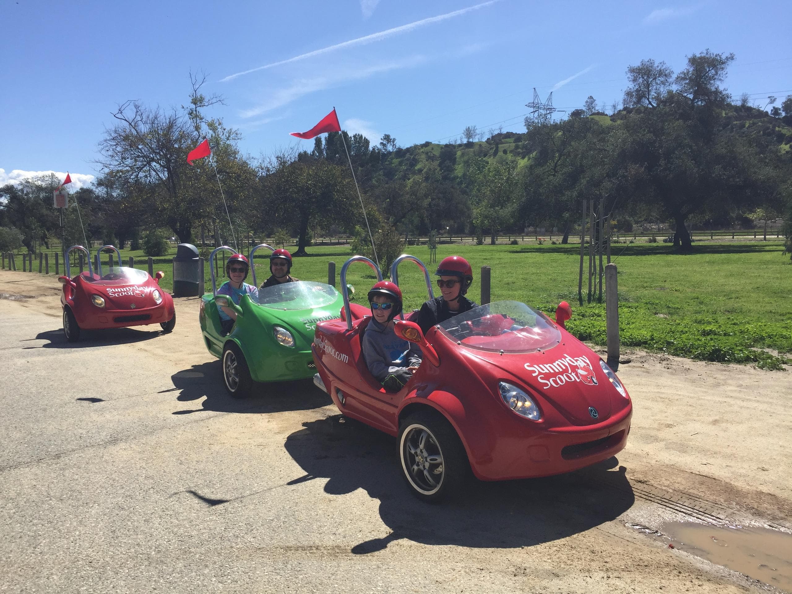 Convoy of red and green scooters driving through sunny park