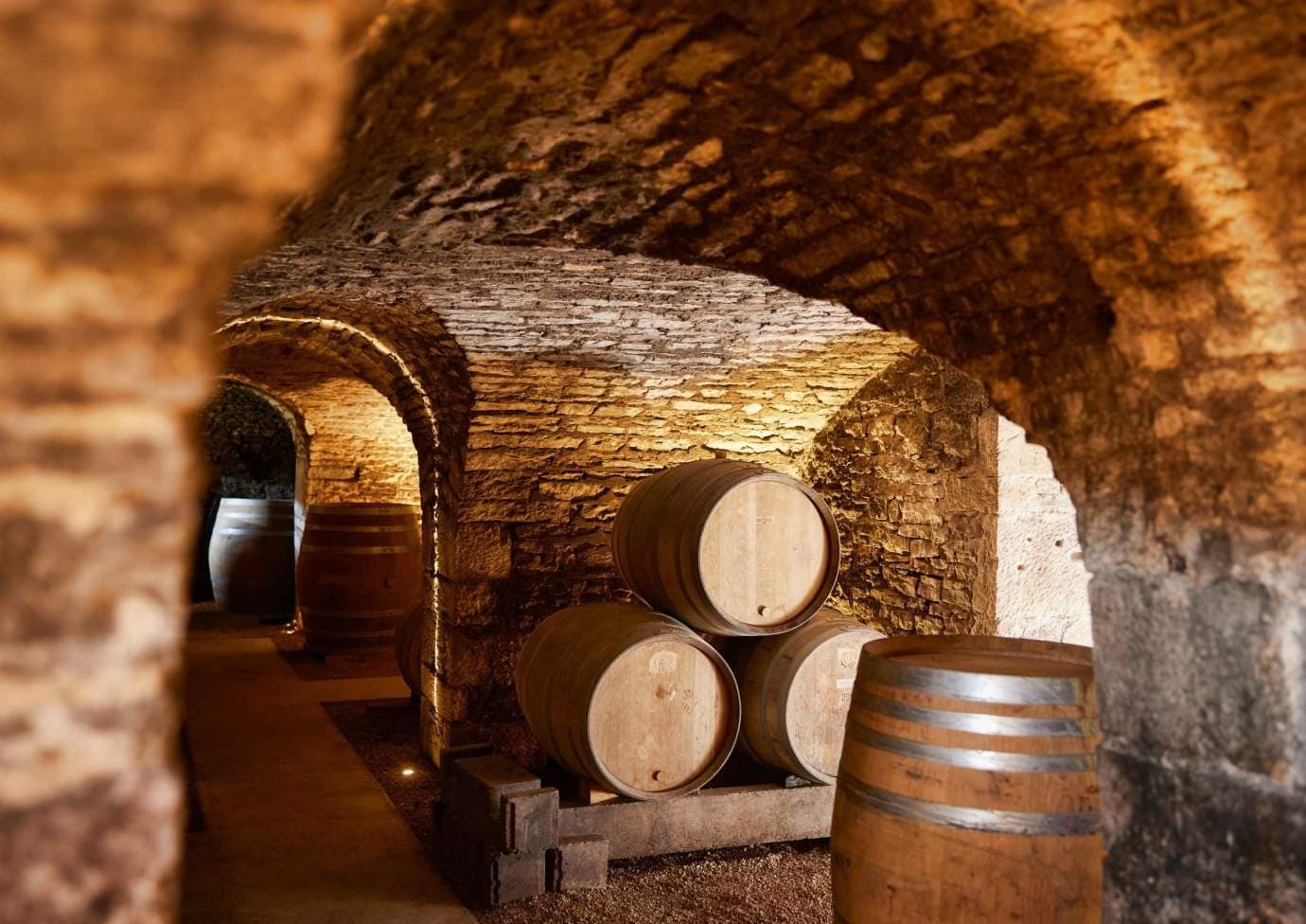 Wine barrels aging in stone cellar tunnel at chateau winery