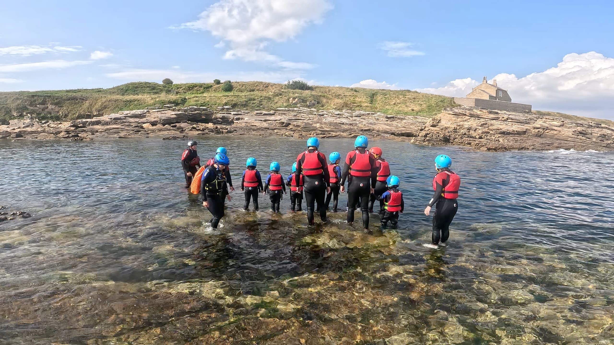 Wetsuited group wading over rocky shoreline during surf session