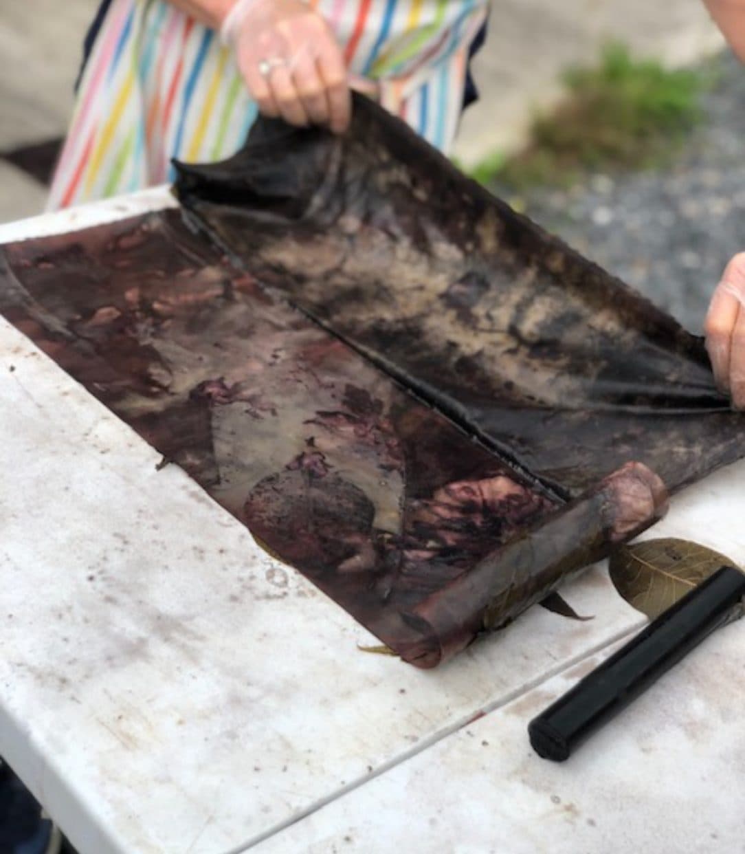 Artist lifting inked print sheet on outdoor table, experimental printmaking