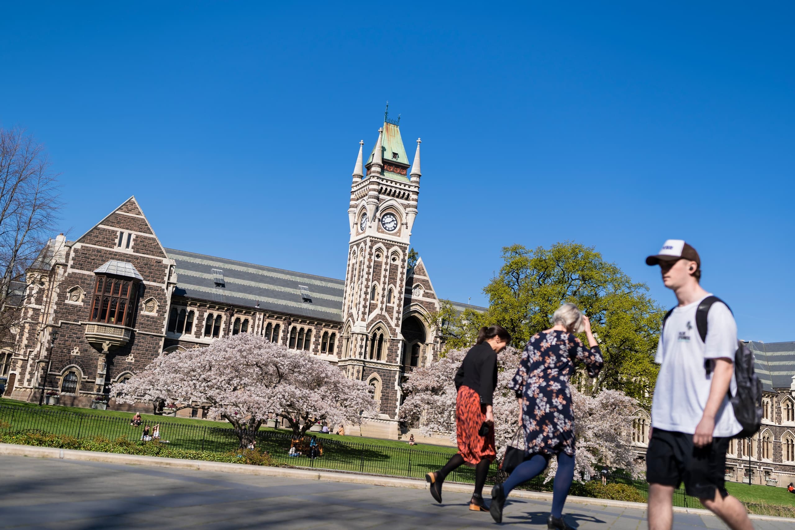Students walking past historic university clocktower on campus lawn