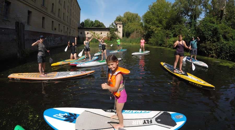 Group paddleboarding through tranquil town canal with buildings