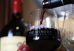 Red wine being poured into glass at indoor winery tasting