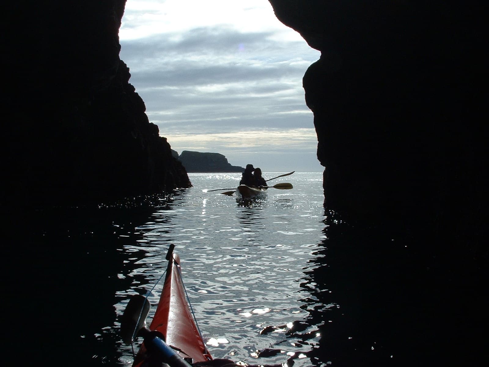 Silhouetted paddlers exiting sea cave into open ocean light