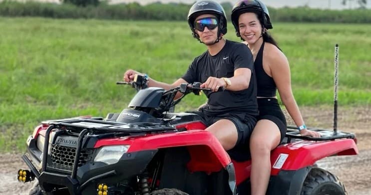 Couple on red ATV in grassy field under open sky smiling