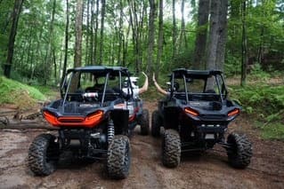 Two off-road UTVs parked in green forest after muddy trail ride